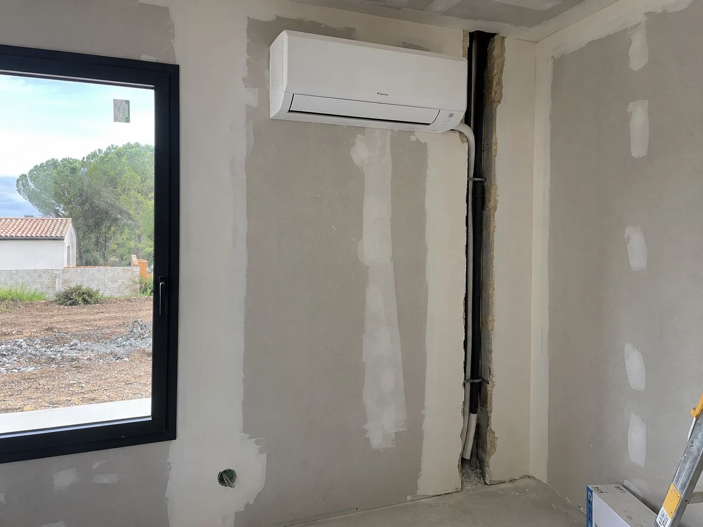 Unité intérieure murale de climatisation réversible posée dans une maison en cours de finition, liaisons dans la cloison