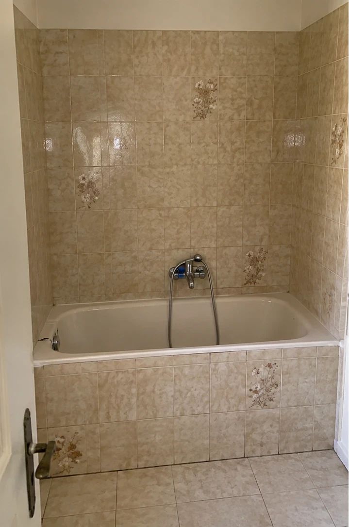 Avant : salle de bain avec baignoire encastrée et faïence beige à motifs floraux
